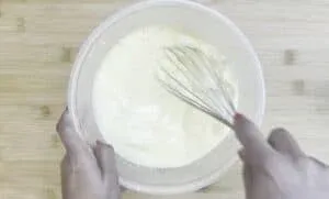 Whisking cake batter in a clear bowl on a wooden surface for a delicious homemade dessert.